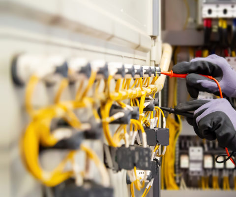 Electrical engineer using digital multi-meter measuring equipment to checking electric current voltage at circuit breaker and cable wiring system in main power distribution board.